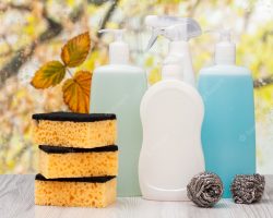 plastic-bottles-dishwashing-liquid-tile-cleaner-detergent-microwave-ovens-stoves-sponges-front-window-with-water-drops-autumn-leaves-washing-cleaning-concept_393202-8556
